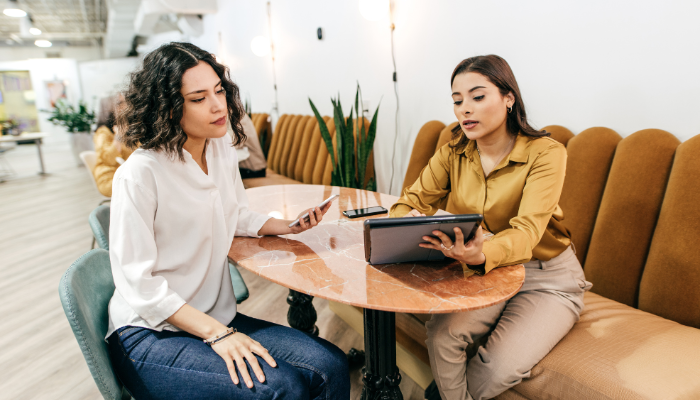 Two women reviewing information on a tablet while one holds a phone.
