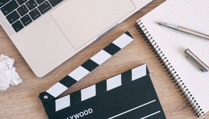 A Hollywood clapboard next to a laptop and pad of paper with a pen sitting on it.